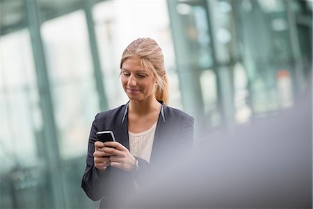 A Young Blonde Businesswoman On A New York City Street. Wearing A Black Jacket. Using A Smart Phone. Stock Photo - Premium Royalty-Free, Code: 6118-07121953