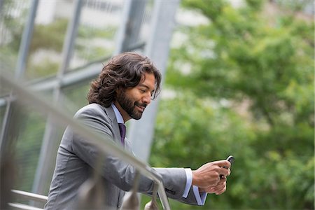 smartphone outdoors - Business People. A Man In A Suit With Brown Curly Hair And A Beard. On His Phone. Stock Photo - Premium Royalty-Free, Code: 6118-07121920