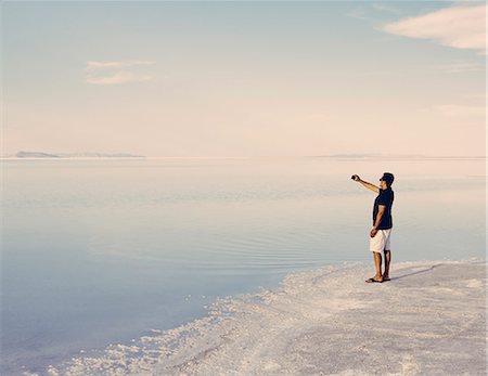 A Man Standing At Edge Of The Flooded Bonneville Salt Flats At Dusk, Taking A Photograph With A Smart Phone Foto de stock - Sin royalties Premium, Código: 6118-07122064