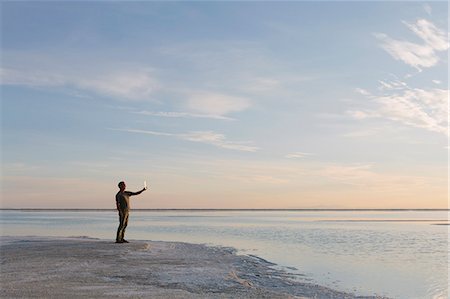 flood - A Man Standing At Edge Of The Flooded Bonneville Salt Flats At Dusk, Taking A Photograph With A Tablet Device. Photographie de stock - Premium Libres de Droits, Code: 6118-07122076