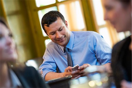 smart phone and texting and business and city - Business People. Three People Around A Cafe Table, One Of Whom Is Checking Their Phone. Stock Photo - Premium Royalty-Free, Code: 6118-07122016