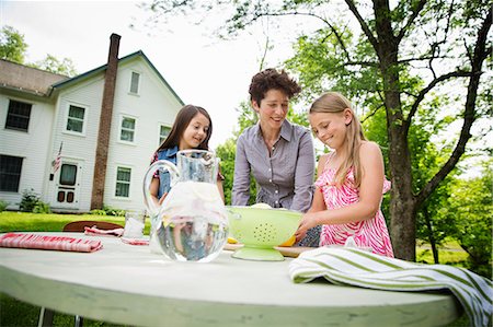 simsearch:6118-07122241,k - A Summer Family Gathering At A Farm. A Woman And Two Children Standing Outside By A Table, Laying The Table. Making Lemonade. Stock Photo - Premium Royalty-Free, Code: 6118-07122147