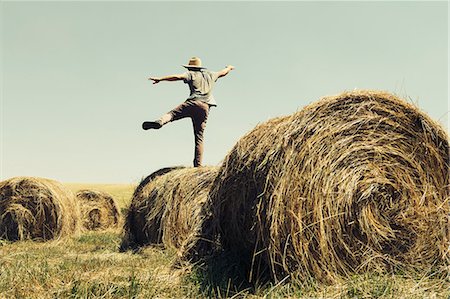 straw (dry vegetation or crop) - Back View Of A Man Balancing On One Leg On Top Of A Hay Bale. Stock Photo - Premium Royalty-Free, Code: 6118-07122116