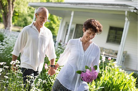 Organic Farm. Summer Party. A Mature Couple In White Shirts Walking Holding Hands Through The Garden. Stock Photo - Premium Royalty-Free, Code: 6118-07122126