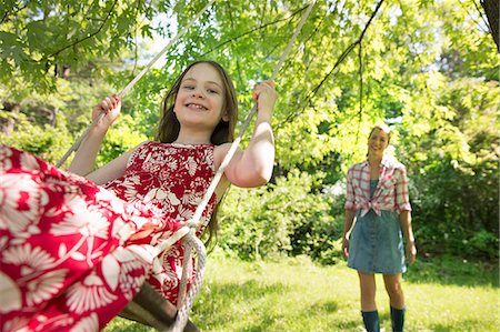 Summer. A Girl In A Sundress On A Swing Under A Leafy Tree. A Woman Standing Behind Her. Stock Photo - Premium Royalty-Free, Code: 6118-07122207