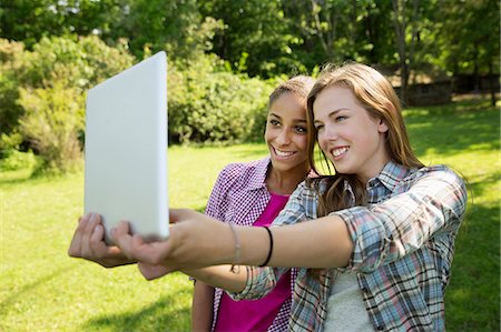 Two Girls Sitting Outdoors On A Bench, Using A Digital Tablet. Holding It Out At Arm's Length. Foto de stock - Sin royalties Premium, Código: 6118-07122217