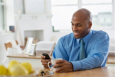 A Man In A Blue Shirt, Sitting At A Breakfast Bar Using A Smart Phone. Foto de stock - Sin royalties Premium, Código: 6118-07122393
