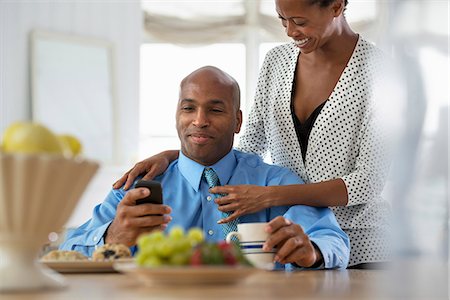 simsearch:6118-07351466,k - A Man In A Blue Shirt, Sitting At A Breakfast Bar Using A Smart Phone. Foto de stock - Sin royalties Premium, Código: 6118-07122392