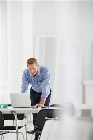 simsearch:6118-07122560,k - Business. A Man Standing Over A Desk, Leaning Down To Use A Laptop Computer. Stock Photo - Premium Royalty-Free, Code: 6118-07122540