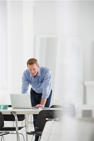 simsearch:6118-07122618,k - Business. A Man Standing Over A Desk, Leaning Down To Use A Laptop Computer. Foto de stock - Sin royalties Premium, Código: 6118-07122540