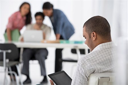 simsearch:6118-07122618,k - Business. A Man Seated In The Foreground, And Three People Working At A Laptop. Foto de stock - Sin royalties Premium, Código: 6118-07122572