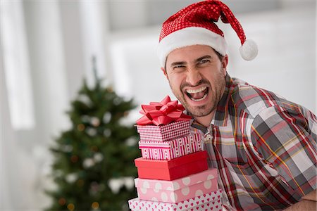 Office Interior. Celebrating Christmas. A Man In A Santa Hat Holding A Stack Of Presents. Decorated Christmas Tree. Photographie de stock - Premium Libres de Droits, Code: 6118-07122661