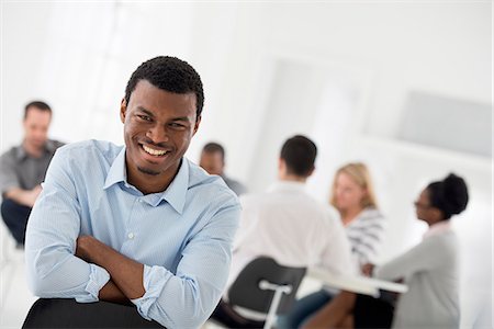 simsearch:6118-07122661,k - Office Interior. A Man Seated With His Armed Folded, Looking Into The Camera. A Group Of People At A Table In The Background. Foto de stock - Sin royalties Premium, Código: 6118-07122689