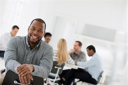 simsearch:6118-07354760,k - Office Interior. A Man Seated Separately From A Group Of People Seated Around A Table. A Business Meeting. Stock Photo - Premium Royalty-Free, Code: 6118-07122693