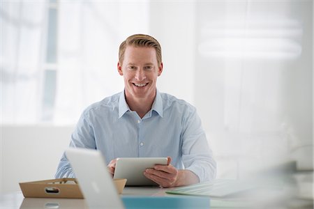 Business. A Light Airy Office Environment. A Man Sitting Holding A Digital Tablet. Photographie de stock - Premium Libres de Droits, Code: 6118-07122601