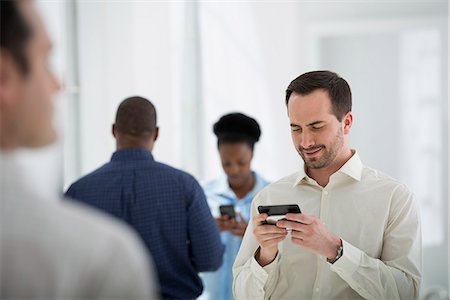 Office Interior. A Group Of People, One Man Using A Smart Phone. Photographie de stock - Premium Libres de Droits, Code: 6118-07122639