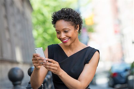 simsearch:6118-07122812,k - People On The Move. A Woman In A Black Dress On A City Street, Checking Her Phone. Stock Photo - Premium Royalty-Free, Code: 6118-07122779