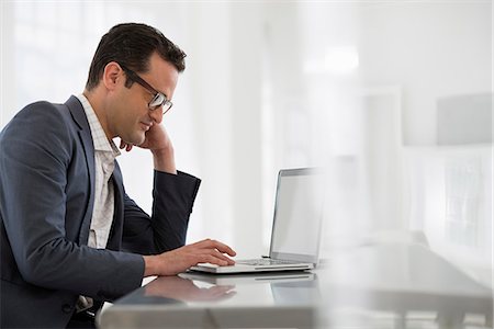 Office Interior. A Businessman Seated At A Table, Using A Laptop Computer. Stockbilder - Premium RF Lizenzfrei, Bildnummer: 6118-07122713