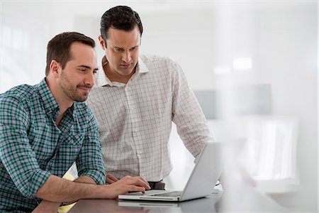 Office Interior. Two Men Standing At A Table Using A Laptop Computer. Stock Photo - Premium Royalty-Free, Code: 6118-07122727