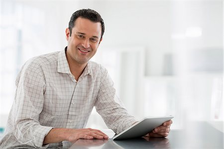 Office Interior. A Man Seated At A Table, Using A Digital Tablet. Stock Photo - Premium Royalty-Free, Code: 6118-07122730