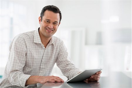 Office Interior. A Man Seated At A Table, Using A Digital Tablet. Photographie de stock - Premium Libres de Droits, Code: 6118-07122730