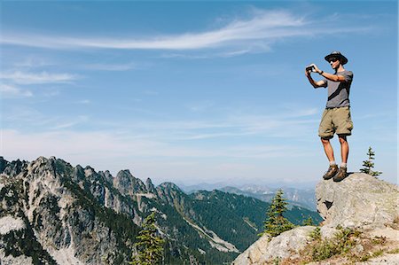 A hiker on a mountain summit, holding a smart phone, at the top of Surprise Mountain, in the Alpine Lakes Wilderness, in Mount Baker-Snoqualmie National Forest. Photographie de stock - Premium Libres de Droits, Code: 6118-07202944