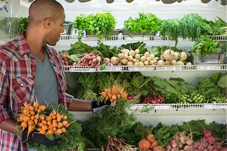 supermarkt - A farm stand with rows of freshly picked vegetables for sale. A man holding bunches of carrots. Stockbilder - Premium RF Lizenzfrei, Bildnummer: 6118-07202988