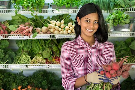A farm stand with rows of freshly picked vegetables for sale. A woman holding a bunch of carrots. Foto de stock - Sin royalties Premium, Código: 6118-07202990