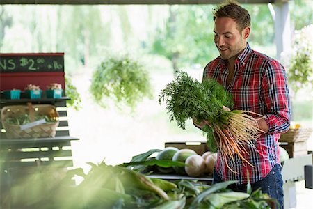 simsearch:6118-07203028,k - A farm stand with fresh organic vegetables and fruit. A man holding bunches of carrots. Photographie de stock - Premium Libres de Droits, Code: 6118-07202992