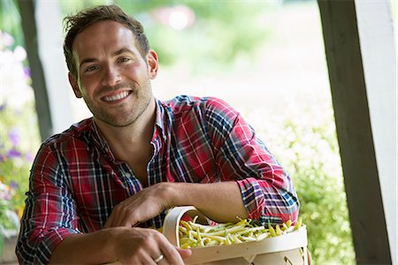 A farm stand with fresh organic vegetables and fruit. A man holding a full basket of beans. Photographie de stock - Premium Libres de Droits, Code: 6118-07203001