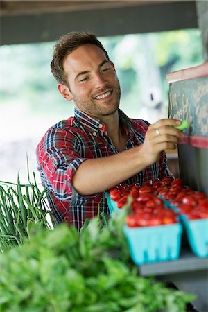 An organic fruit stand. A man chalking up prices on the blackboard. Stock Photo - Premium Royalty-Free, Code: 6118-07203006