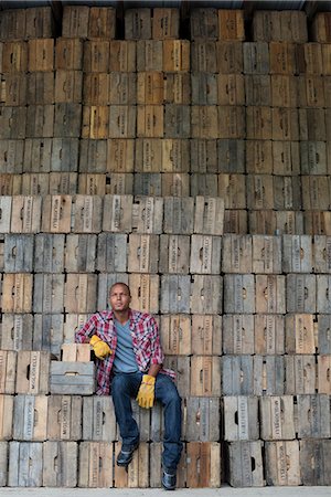 A farmyard. A stack of traditional wooden crates for packing fruit and vegetables. A man sitting on a packing case. Photographie de stock - Premium Libres de Droits, Code: 6118-07203026