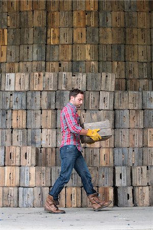 A farmyard. A stack of traditional wooden crates for packing fruit and vegetables. A man carrying an empty crate. Stockbilder - Premium RF Lizenzfrei, Bildnummer: 6118-07203029
