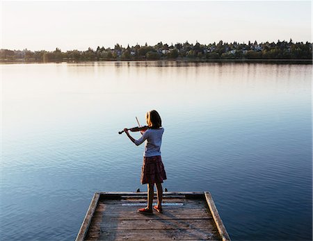 A ten year old girl playing the violin at dawn on a wooden dock. Photographie de stock - Premium Libres de Droits, Code: 6118-07203251
