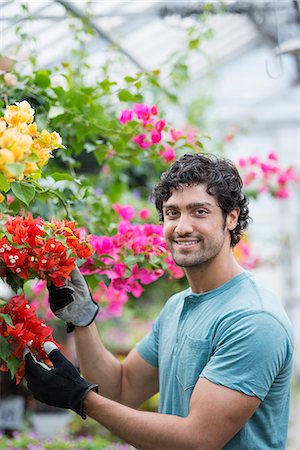 simsearch:6118-07203002,k - A young man working in a greenhouse full of flowering plants. Foto de stock - Sin royalties Premium, Código: 6118-07203367