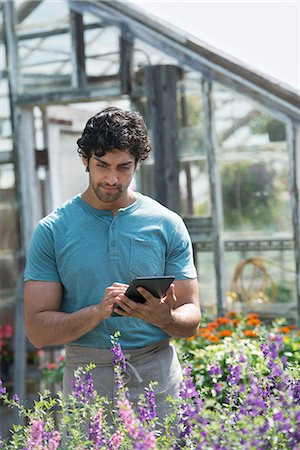 A young man working in a plant nursery, surrounded by flowering plants. Stock Photo - Premium Royalty-Free, Code: 6118-07203384