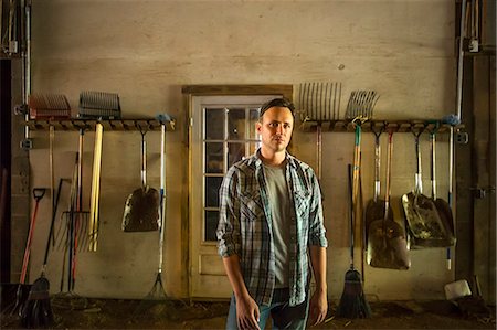 stable - An organic farm in the Catskills. A man standing in a barn with equipment stored around the walls. Stock Photo - Premium Royalty-Free, Code: 6118-07203326