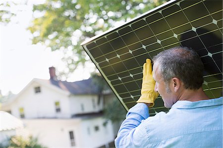diy or home improvement - A man carrying a solar panel towards a building under construction. Foto de stock - Sin royalties Premium, Código: 6118-07203461