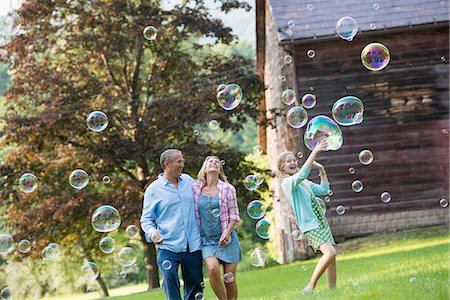 A family sitting on the grass outside a bar, blowing bubbles and laughing. Foto de stock - Sin royalties Premium, Código: 6118-07203466