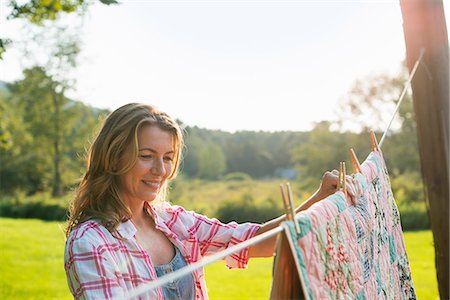 A woman hanging laundry on the washing line, in the fresh air. Stock Photo - Premium Royalty-Free, Code: 6118-07203412