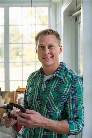 A man in a workshop, holding a carpenter's clamp in his hand. Stock Photo - Premium Royalty-Free, Code: 6118-07203415