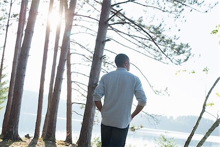 simsearch:6118-07203926,k - Lakeside. A man standing in the shade of pine trees in summer. Foto de stock - Sin royalties Premium, Código: 6118-07203562