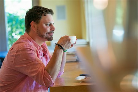 A man sitting at a cafe table, holding a cup of coffee. Stock Photo - Premium Royalty-Free, Code: 6118-07203571