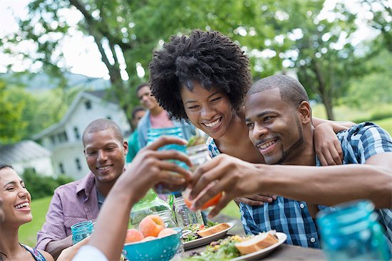 A group of adults and young people at a meal in the garden of a farmhouse. Passing plates and raising glasses. Stock Photo - Premium Royalty-Free, Image code: 6118-07203745