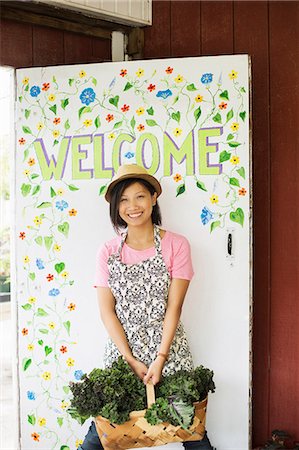 simsearch:6118-07202987,k - Working on an organic farm. A young Asian woman by the Welcome sign with a large basket of vegetables, freshly picked. Stock Photo - Premium Royalty-Free, Code: 6118-07203873