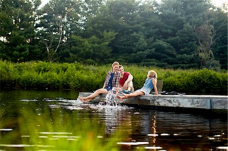 Three people, two adults and a child relaxing on a jetty, with their feet in the water at the end of a day. Stockbilder - Premium RF Lizenzfrei, Bildnummer: 6118-07203940