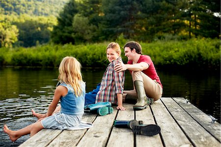 Three people, two adults and a child relaxing on a jetty, with their feet in the water at the end of a day. Stock Photo - Premium Royalty-Free, Code: 6118-07203939