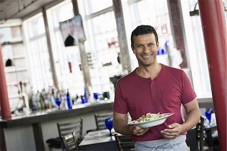 A cafe interior. A man in a waiter's apron serving a meal. Stock Photo - Premium Royalty-Free, Code: 6118-07235087