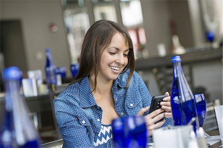 A woman seated in a cafe using a smart phone. Stock Photo - Premium Royalty-Free, Code: 6118-07235089