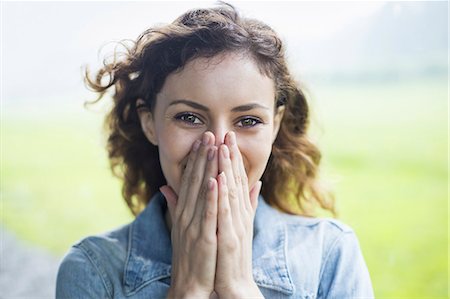 A young woman in a rural landscape, with windblown curly hair. Covering her face with her hands, and laughing. Photographie de stock - Premium Libres de Droits, Code: 6118-07235183